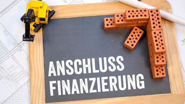 Miniziegelsteine und Kreidetafel mit Bauplan und Wort Anschlussfinanzierung