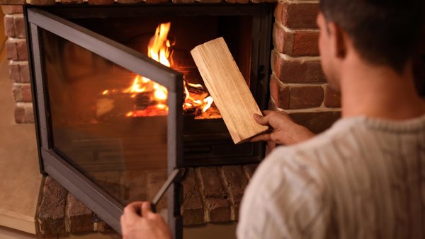 Ein Mann legt Feuerholz im heimischen Kaminofen nach