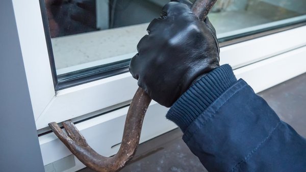 Behandschuhte Hand mit Brecheisen bricht Fenster auf