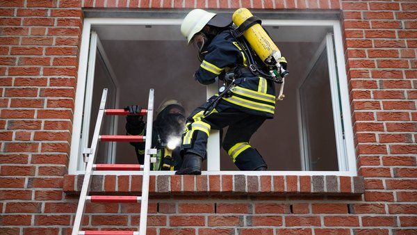 Feuerwehrmann mit Atemschutz klettert über eine Leiter in ein Gebäude